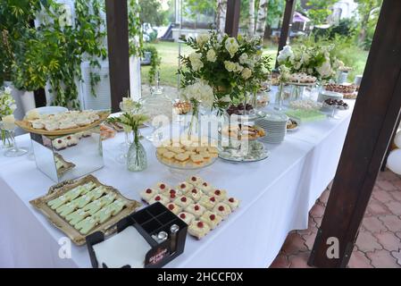 Table de banquet de gâteaux joliment décorés avec bouquets de fleurs sur une nappe prête pour un événement Banque D'Images