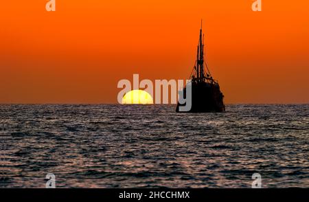 Le coucher du soleil est Une silhouette d'Un bateau à voile reposant sur la mer tandis que le soleil se trouve sur l'horizon océanique Banque D'Images