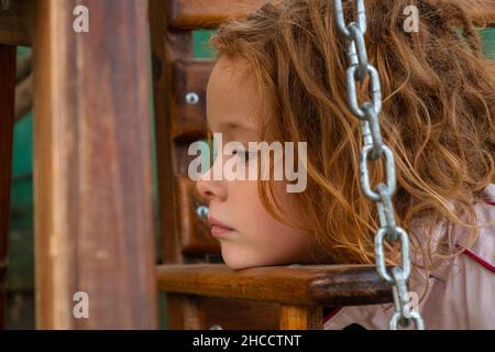 petite belle fille aux cheveux rouges regarde pensivement dans la distance, gros plan portrait. Banque D'Images