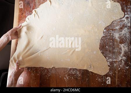 Vue de dessus d'une femme tirant de la pâte vegan roulée maison sur une table à manger saupoudrée de farine. Banque D'Images