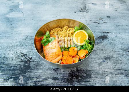 Portion de saumon grillé compotée de quinoa cuit, d'arugula, de persil et de carottes dans un bol en métal Banque D'Images