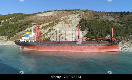 Antenne pour navire de fret rouge industriel sur la rive bleue de la mer avec beaucoup de personnes marchant.Grande barge amarrée sur la rive de la mer près d'une pente recouverte d'un arbre vert Banque D'Images