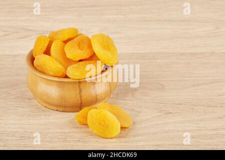 Assiette en bois remplie d'abricots séchés sur fond de bois, à côté d'abricots secs épars Banque D'Images