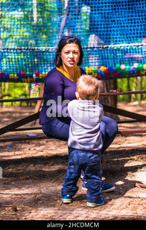 Femme assise sur un banc en bois à côté d'un enfant dans le parc Pyrlandia. Banque D'Images