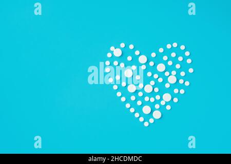 Pilules blanches rondes de différentes tailles en forme de coeur sur fond bleu.Concept d'amour et de soins de santé.Pose à plat.Copier l'espace.Minimalisme.Maquette. Banque D'Images