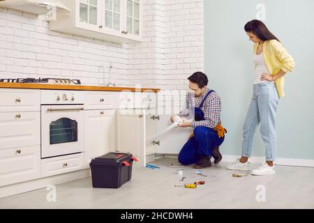 Plombier de résoudre certains problèmes avec l'évier drain dans la cuisine d'une jeune femme maison Banque D'Images