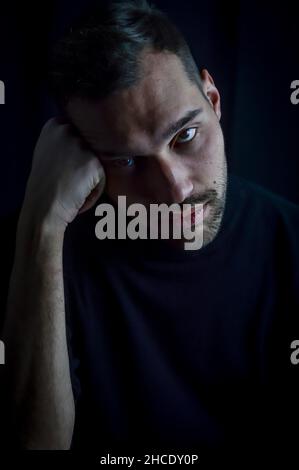 portrait d'un jeune homme avec sa tête reposant sur son poing regardant très ennuyé et déprimé Banque D'Images