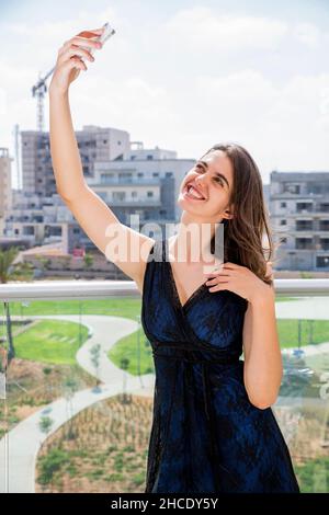 Jeune femme en robe de soirée prend un selfie à l'extérieur Banque D'Images
