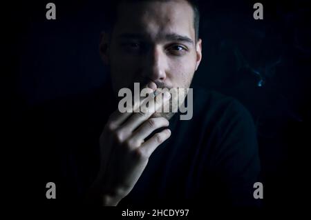 gros plan portrait d'un jeune homme qui fume en tenant les derniers coups de la cigarette dans sa main Banque D'Images