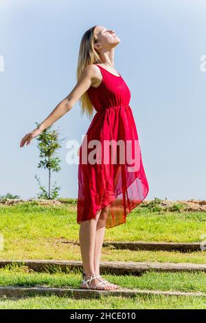La jeune femme en robe rouge apprécie l'air frais dehors Banque D'Images