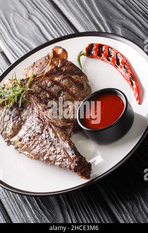 Le portreuse en T grillé est un steak de bœuf coupé à partir du petit loin dans l'assiette de la table noire.Verticale Banque D'Images