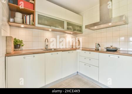 Intérieur de cuisine moderne meublée avec armoires blanches minimalistes et comptoir en bois avec cuisinière intégrée et hotte aspirante Banque D'Images