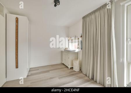 Spacieuse et lumineuse, cette chambre pour enfants est meublée d'une table à langer et d'une garde-robe placée sur du parquet près d'une fenêtre avec des rideaux Banque D'Images