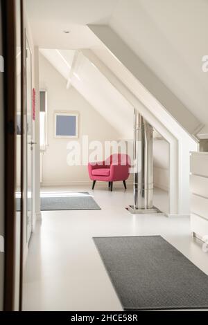 Intérieur d'une spacieuse salle lumineuse sur mansarde avec portes blanches et murs menant à la pièce avec fauteuil rose vif Banque D'Images