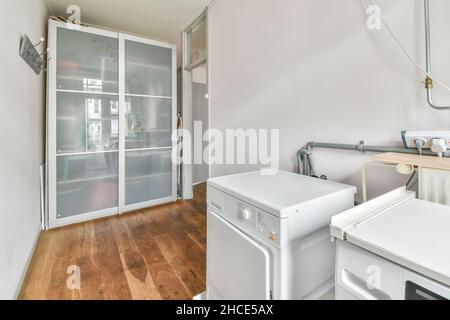 Lave-linge blanc placé sur parquet dans un coin près du mur contre la porte vitrée du balcon à la lumière du jour Banque D'Images