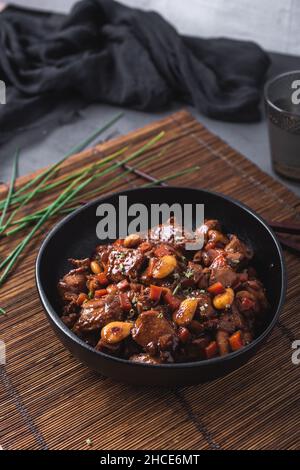 Du dessus du bol avec du poulet asiatique aux amandes et aux légumes placés près des baguettes de bambou et de la ciboulette Banque D'Images