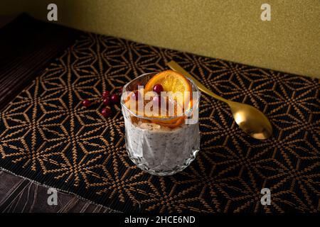 Grand angle de verre de dessert fait de mousse de stracciatella et de copeaux de chocolat recouvert de tranches caramélisées d'orange et de baies près de la cuillère Banque D'Images