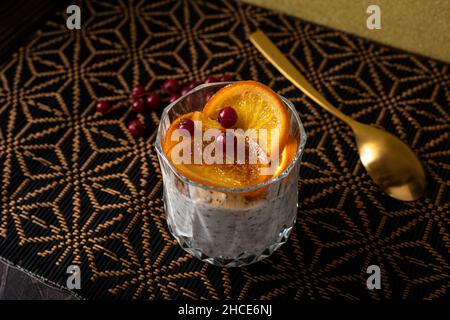 Grand angle de verre de dessert fait de mousse de stracciatella et de copeaux de chocolat recouvert de tranches caramélisées d'orange et de baies près de la cuillère Banque D'Images