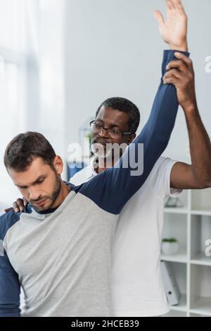 un médecin afro-américain mature qui élève la main du jeune homme tout en l'examinant dans un centre de réadaptation Banque D'Images