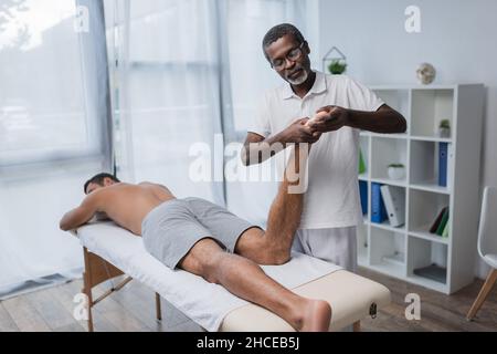 un réhabilitologue afro-américain massante le pied d'un jeune homme en clinique Banque D'Images