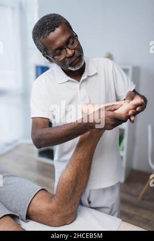 un physiothérapeute afro-américain d'âge moyen massait le pied de l'homme dans un centre de réadaptation Banque D'Images