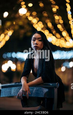 Portrait de mode de la jeune femme asiatique penchée sur une balustrade dans la rue la nuit portant une robe de fête Banque D'Images