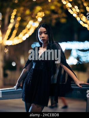 Portrait d'une jeune femme asiatique penchée sur une rampe dans la rue la nuit portant une robe de fête Banque D'Images