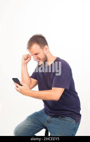 Homme posant avec joie avec un téléphone devant un mur blanc Banque D'Images
