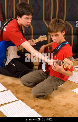 garçon de 13 ans à la maison jouant de la guitare électrique, jouant avec son frère de 12 ans, lui démontrant la corde Banque D'Images