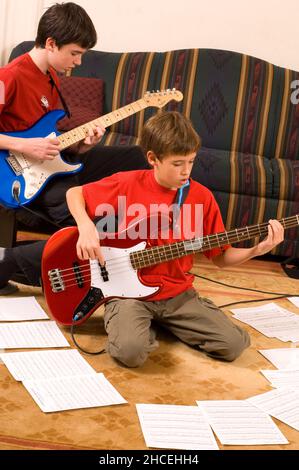 garçon de 13 ans à la maison jouant de la guitare électrique, jouant avec son frère de 12 ans Banque D'Images