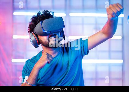 Jeune homme avec VR ou masque de réalité virtuelle ou casque dansant sur la lumière de néon scène arrière - concept de l'expérience technologique moderne. Banque D'Images