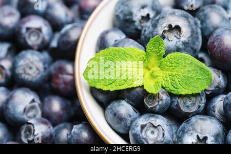 Bleuets frais dans un bol avec fond de feuille de menthe ou toile de fond.Concept végétalien et végétarien.Texture macro des myrtilles.Été en bonne santé Banque D'Images
