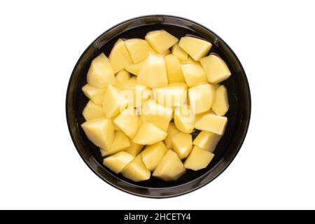 Pommes de terre fraîchement pelées dans une assiette en céramique noire, coupées en morceaux et recouvertes d'eau, vue rapprochée du dessus. Banque D'Images