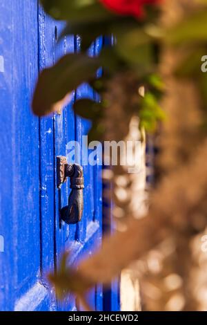 Porte peinte en bleu vif avec un porte en forme de main knocker et couronne de fleurs rouges de plantes d'épines dans une maison dans le village de Chirche, Guia de Isora, Banque D'Images