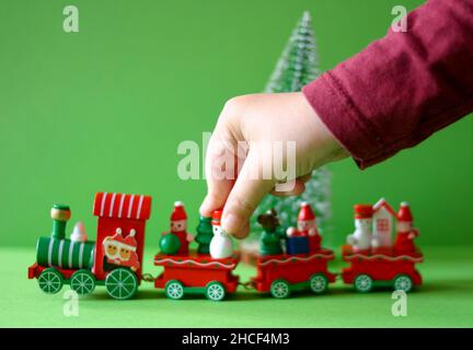 Main de garçon jouant avec un train de jouets de Noël avec des wagons isolés sur un fond vert Banque D'Images