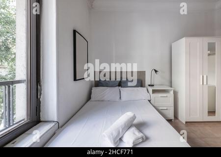 Cette chambre dispose d''un mobilier blanc, d''un lit fraîchement préparé et d''une fenêtre en aluminium avec des portes en bois blanc. Banque D'Images