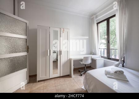 Cette chambre dispose d''un mobilier blanc, d''un lit fraîchement préparé et d''une fenêtre en aluminium avec des portes en bois blanc. Banque D'Images