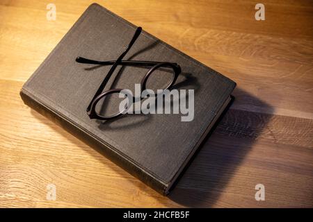 Vieux livre noir fermé sur une table.Ordinateur portable à couverture rigide et lunettes sur fond en bois, vue du dessus.Bureau des enseignants, Banque D'Images