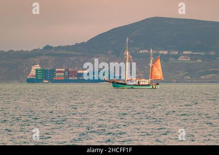 Sandycove, Dublin, Irlande, 13 novembre 2021 : un petit yacht dans la baie de Dublin avec un bateau à conteneurs en arrière-plan. Banque D'Images