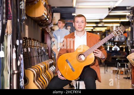 Joyeux vendeur de sexe masculin montrant de la guitare à un client de type garçon Banque D'Images