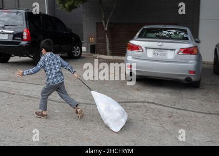 Austin Texas USA, décembre 2021 : un enfant afghan prend des déchets dans une benne à ordures alors que sa famille s'installe dans sa nouvelle maison dans un complexe d'appartements près du centre-ville.Les réfugiés fuyant la tourmente en Afghanistan continuent d'être réinstallés au Texas, avec de nombreux hommes célibataires et de grandes familles avec des enfants qui déménagent dans des appartements à travers Austin.Les groupes religieux et autres groupes à but non lucratif ont intensifié leurs efforts pour coordonner les efforts visant à fournir des maisons à des centaines de réfugiés.©Bob Daemmrich Banque D'Images