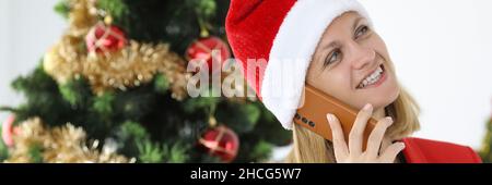 Une femme dans le chapeau du père noël parle au téléphone contre le fond de l'arbre de Noël Banque D'Images