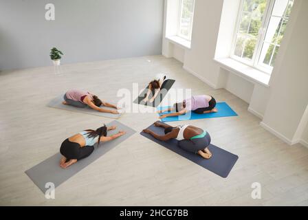 Groupe diversifié de jeunes femmes pratiquant la pose de repos de l'enfant pendant l'entraînement de yoga à la salle de gym Banque D'Images