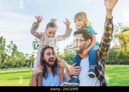 Deux papas joyeux tenant leurs jeunes enfants sur leurs épaules Banque D'Images