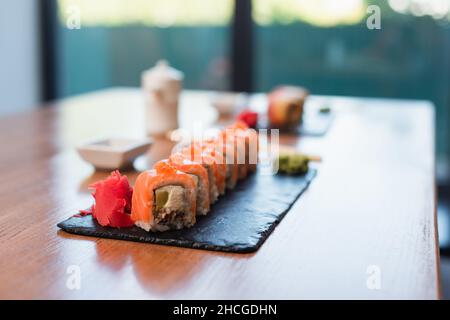 délicieux petits pains à sushis près du gingembre sur une assiette noire et une table en bois, fond flou Banque D'Images