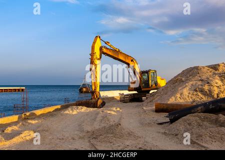 Tracteur avec godet sur la plage.La pelle hydraulique travaille avec la côte. Banque D'Images