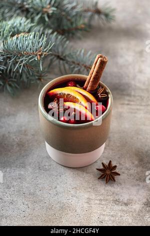 Vigne mutée aux épices, tranches d'orange, canneberge et étoile anis en verre céramique avec une branche d'un arbre de Noël à l'arrière sur fond texturé Banque D'Images