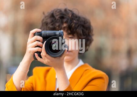 Jeune femme brune aux cheveux bouclés prenant une photo avec son grand appareil photo Banque D'Images