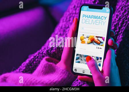 Une femme se trouve sur un canapé tenant un téléphone mobile avec une application d'achat de pharmacie sur Internet.Boutique de pharmacie Mokup.Médical, aide, assistance en ligne.Soins de santé télémédic Banque D'Images