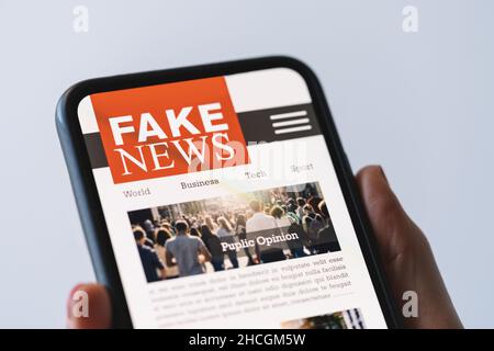 Fausses nouvelles en ligne sur un téléphone portable.Gros plan de la femme lisant des faux CANULARS ou des articles dans une application d'écran de smartphone.Main tenant le dispositif intelligent Banque D'Images
